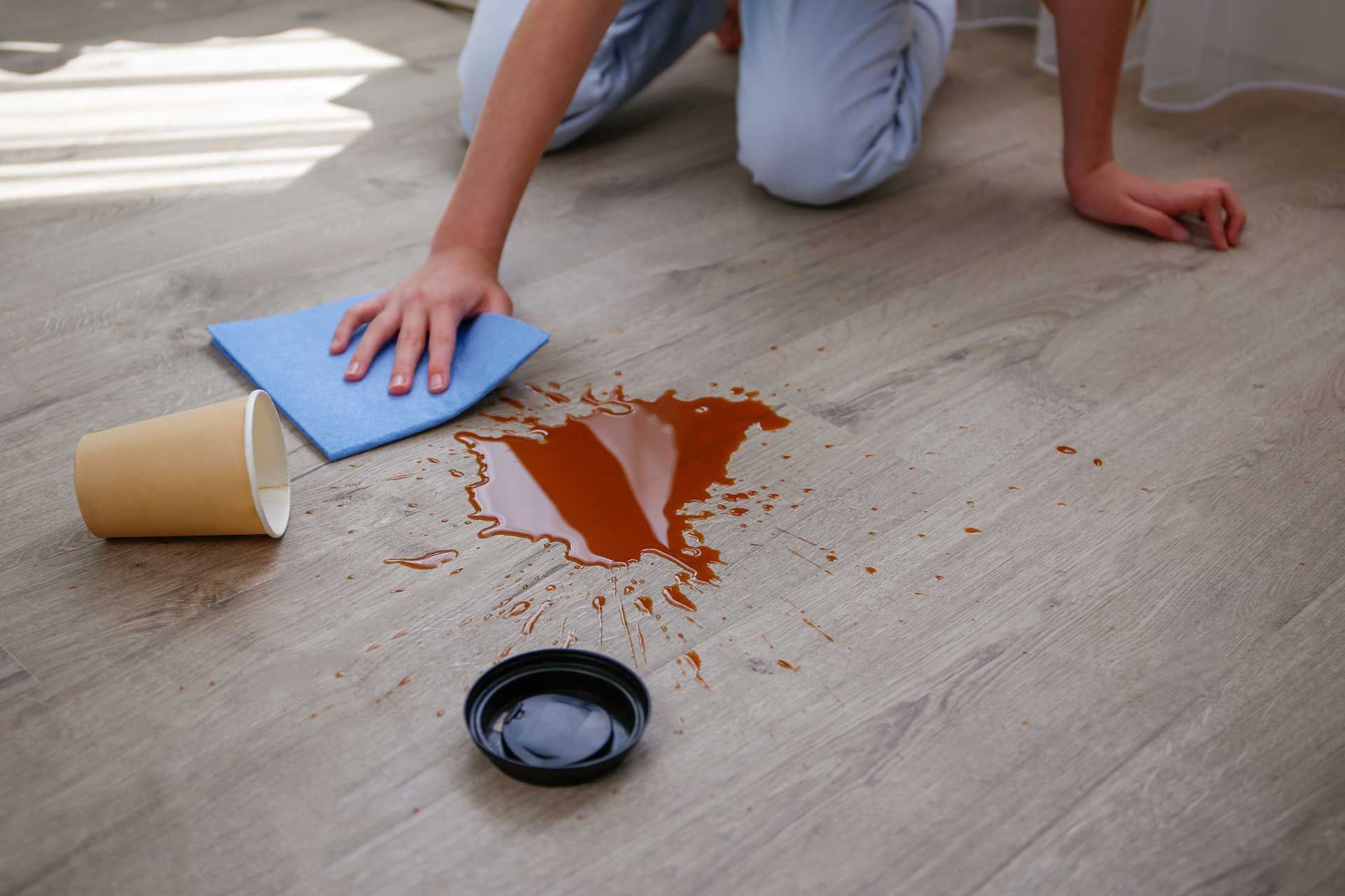 A person is cleaning a spilled cup of coffee on the floor.
