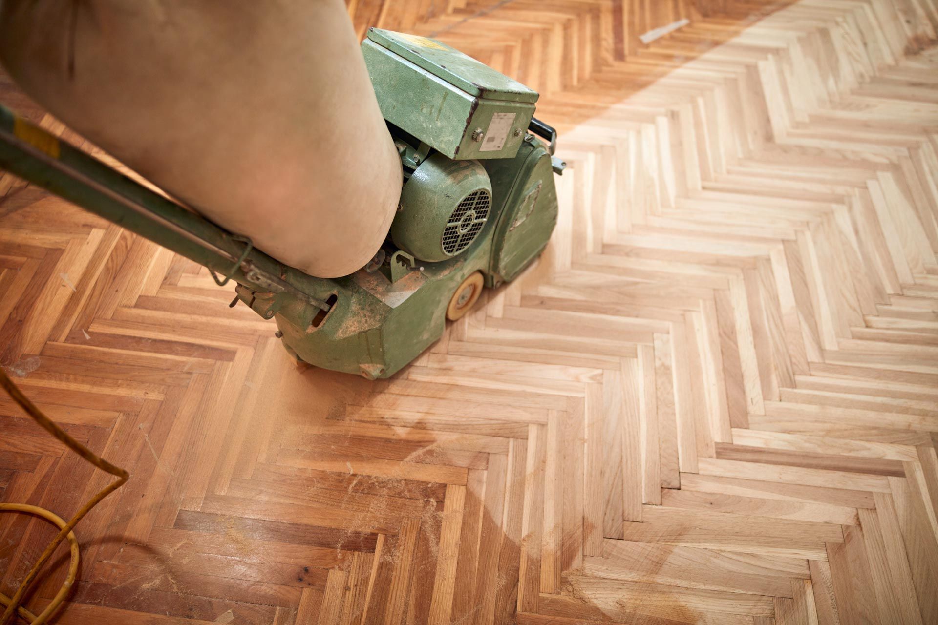 A person is sanding a wooden floor with a machine.
