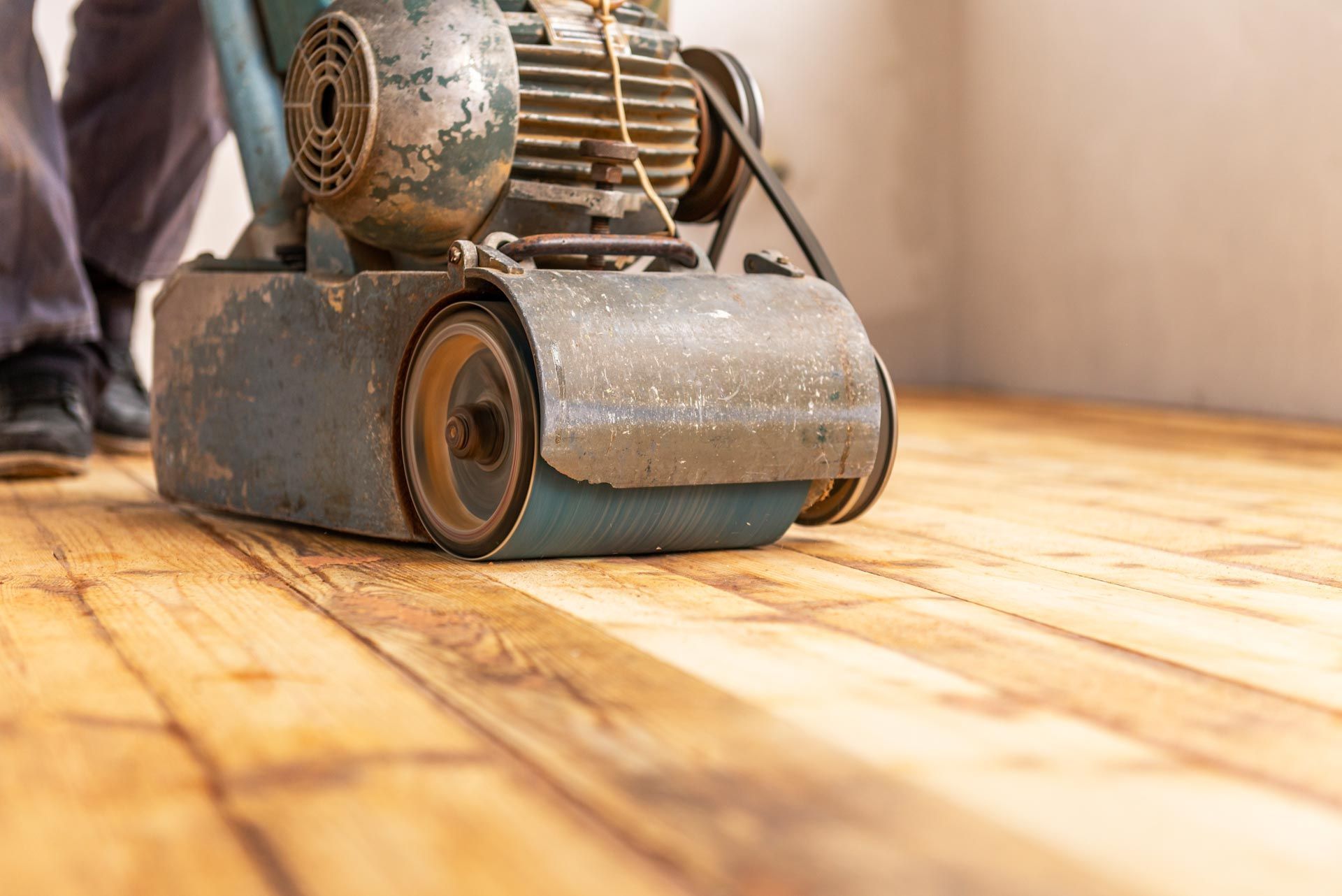 A person is sanding a wooden floor with a machine.