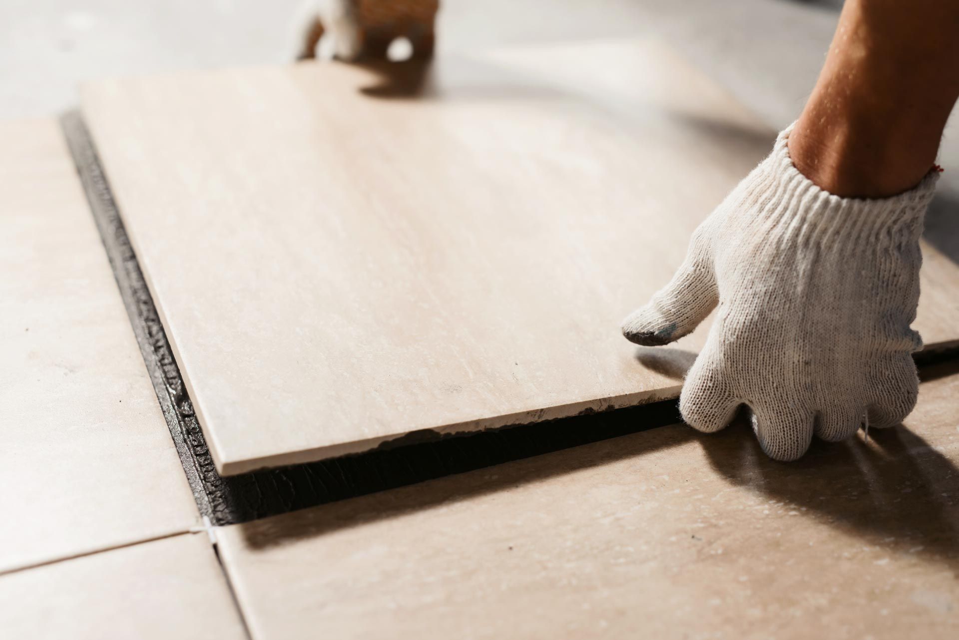 A person wearing gloves is laying a tile on the floor.