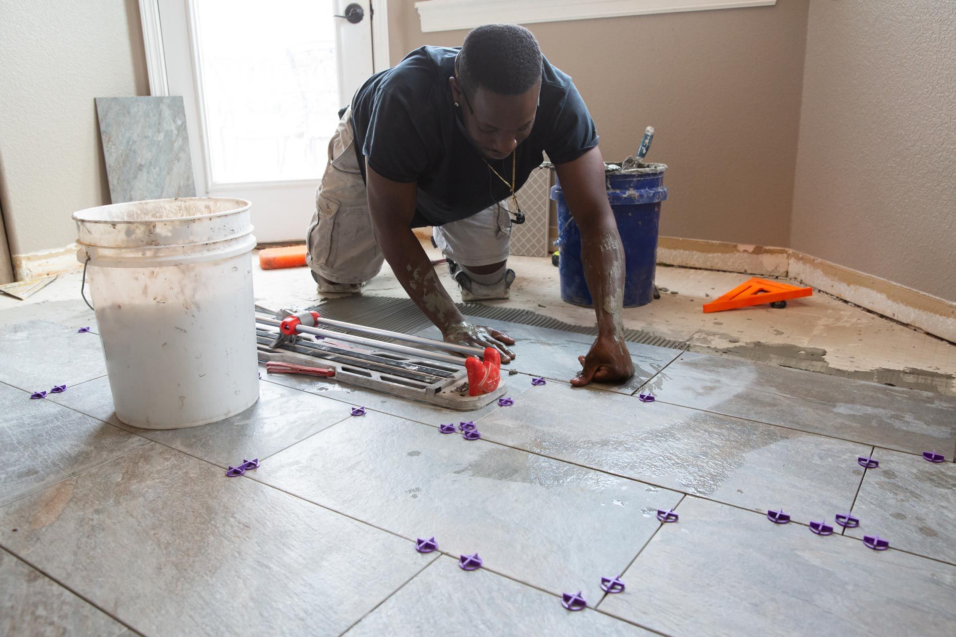 A man is laying tile on the floor in a room.