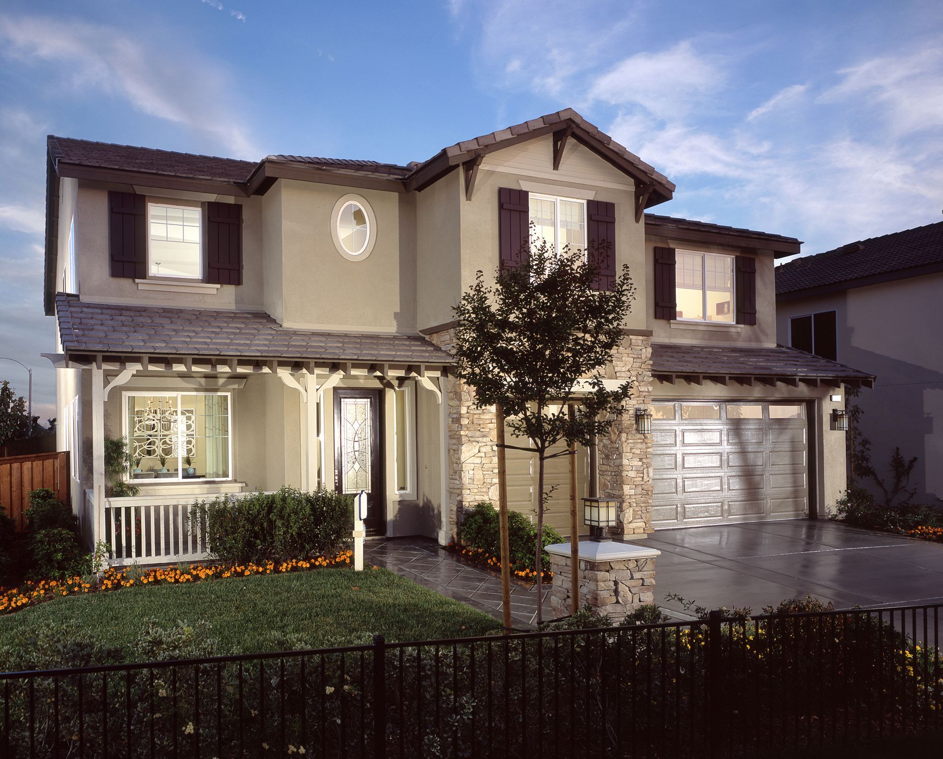 Suburban two-story house with beige siding, lit windows, and a two-car garage at dusk