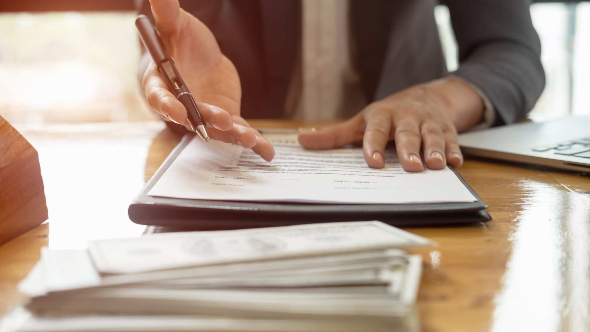 Hand signing a document on a wooden desk with papers stacked in the foreground