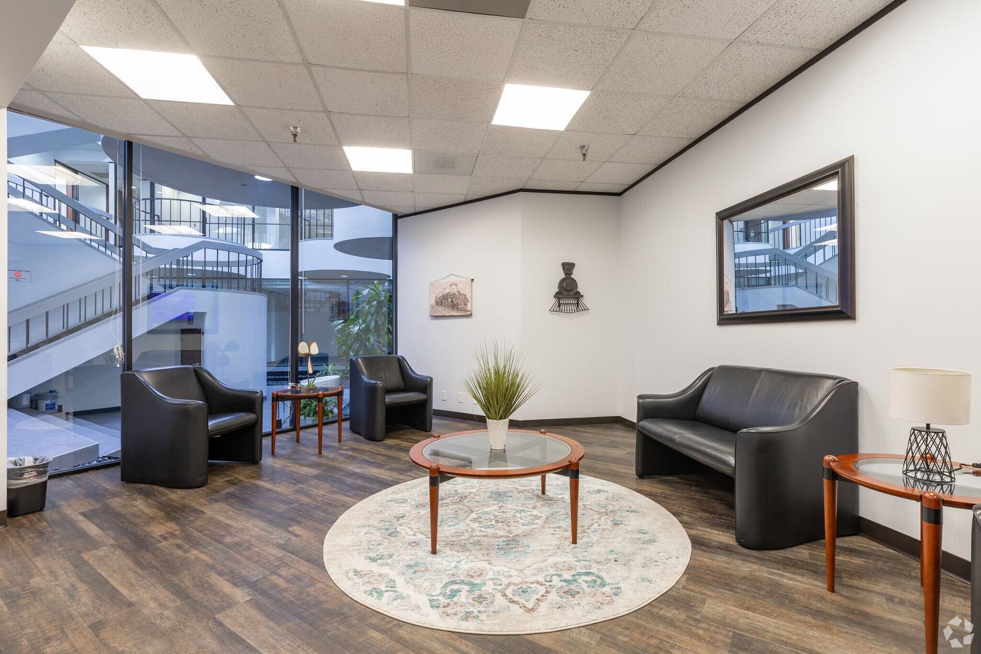 Modern lobby with black chairs, round coffee table, rug, and large windows overlooking stairs