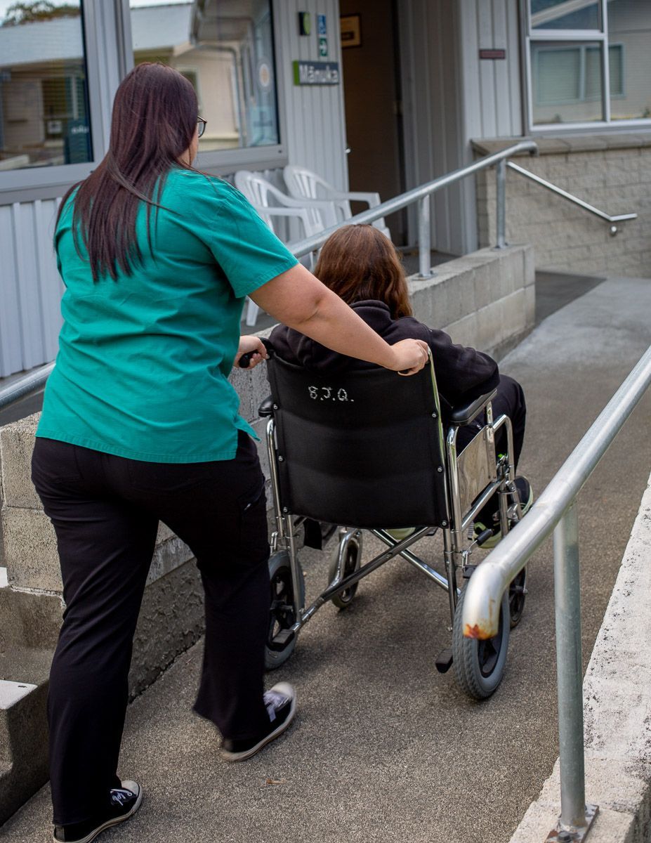 Woman pushing person in wheelchair up a ramp outside a building