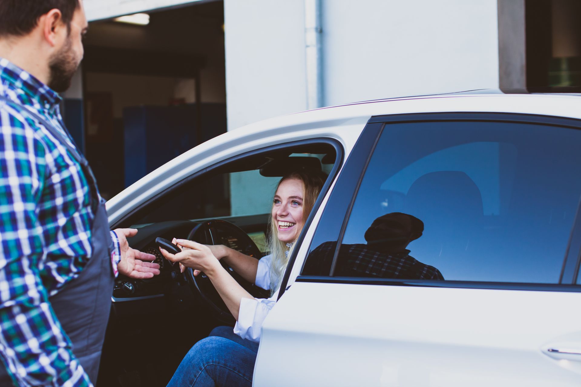 A mechanic handing car keys to a smiling woman sitting in a white car. A mechanic handing car keys to a smiling woman sitting in a white car.