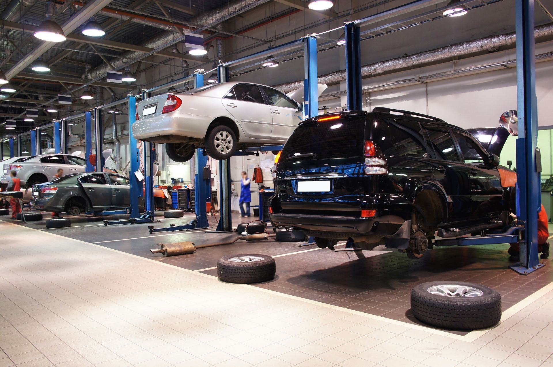 Cars raised on lifts in a busy auto repair shop; mechanics working. Cars raised on lifts in a busy auto repair shop; mechanics working.