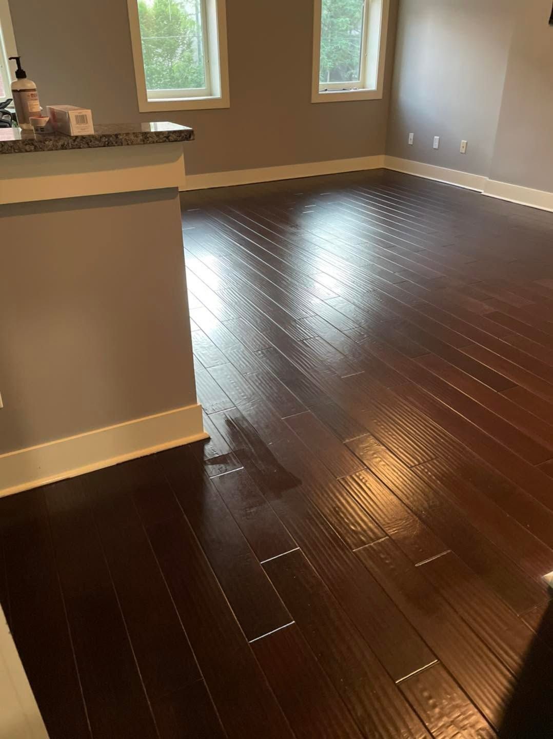 Empty room with dark wood floors and beige walls, lit by two windows.