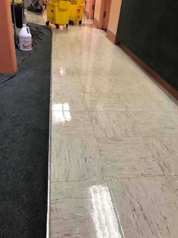 Empty hallway with shiny tiled floor, pink walls, and cleaning supplies in the distance.