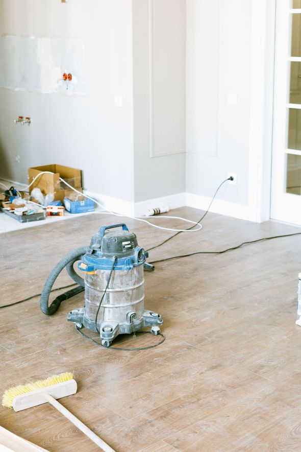 Vacuum cleaner on a dusty carpet in a partially renovated room with tools and debris nearby