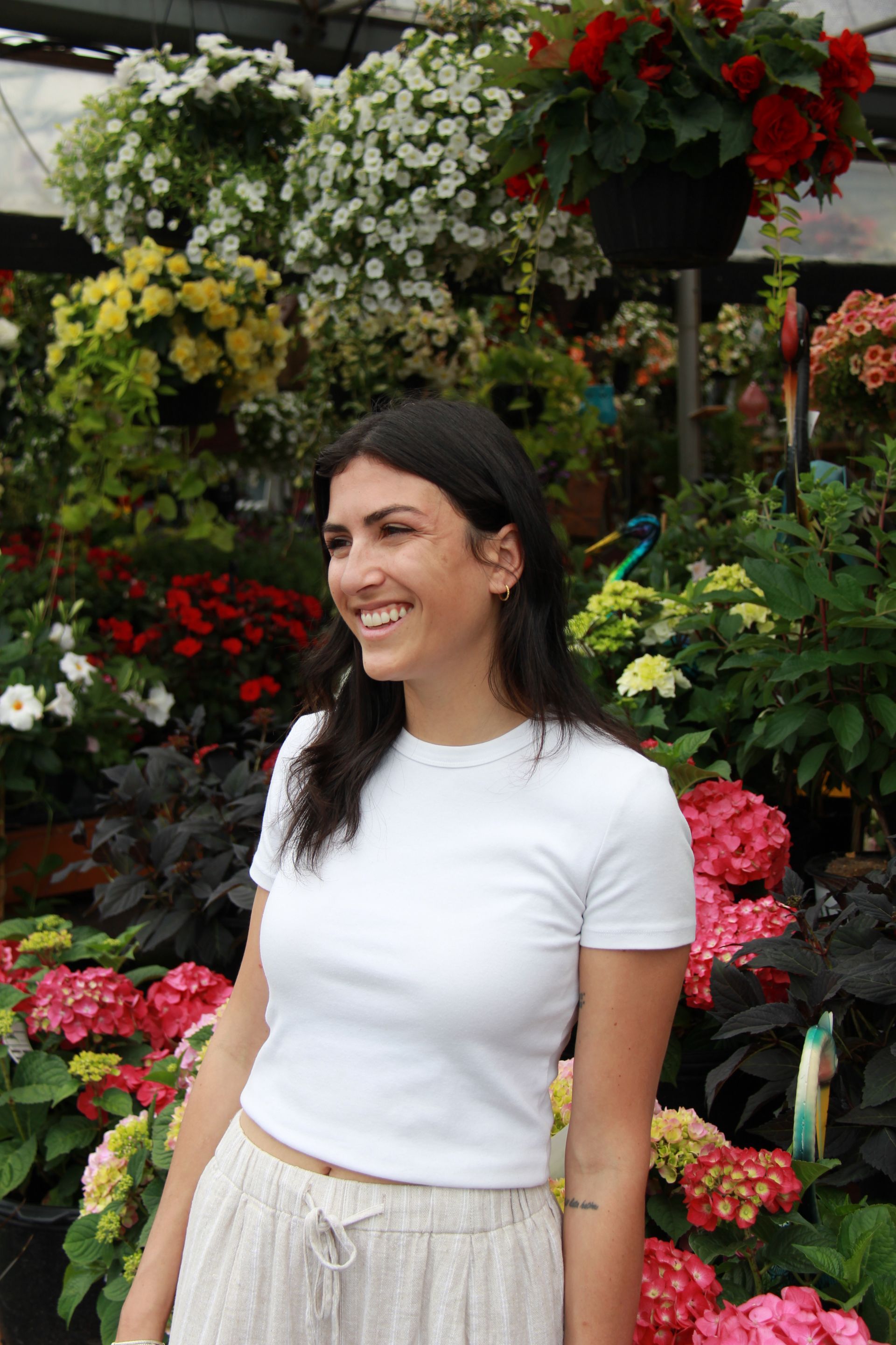 Une personne souriante devant un mur vert ondulé, vêtue d'une chemise rose et d'un tablier noir.