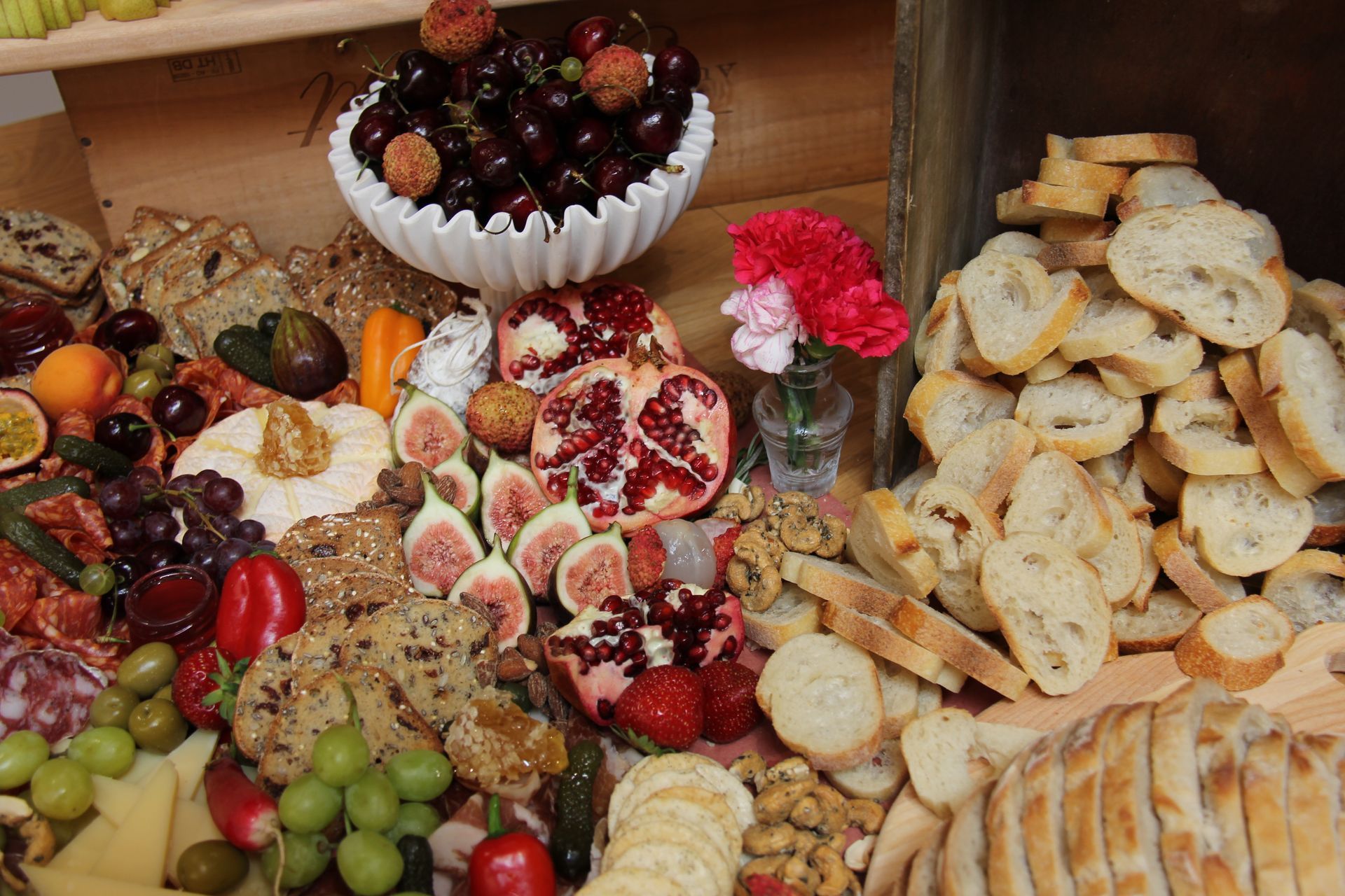 Un assortiment coloré de fruits, légumes, fromages, noix et fleurs disposé sur une table rustique.