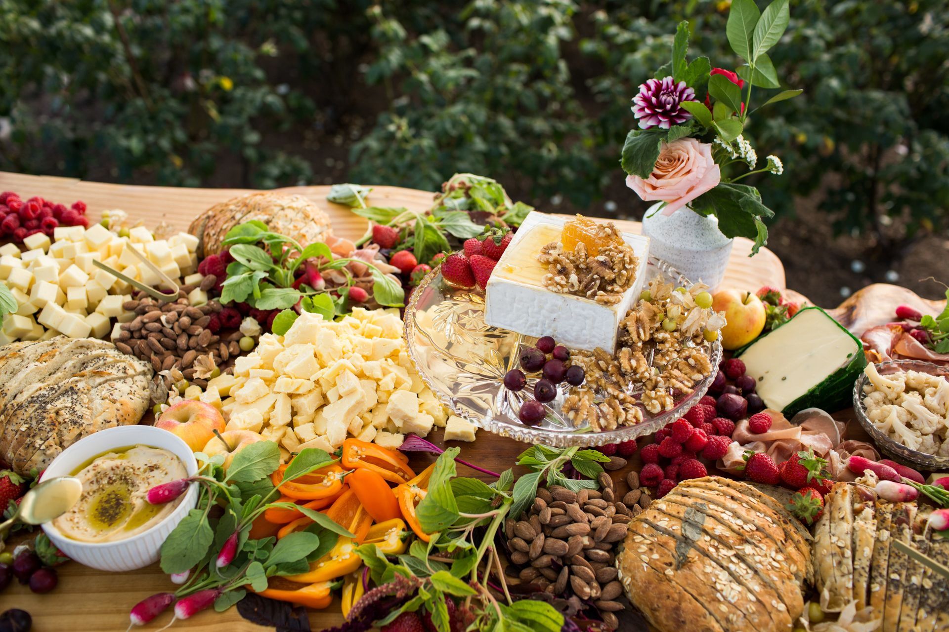 Un assortiment coloré de fruits, légumes, fromages, noix et fleurs disposé sur une table rustique.
