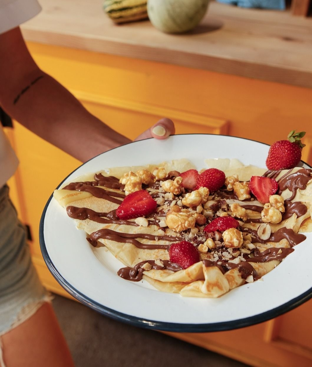 Assiette de crêpes garnies de fraises, de noix et d'un filet de chocolat, présentée dans une cuisine.
