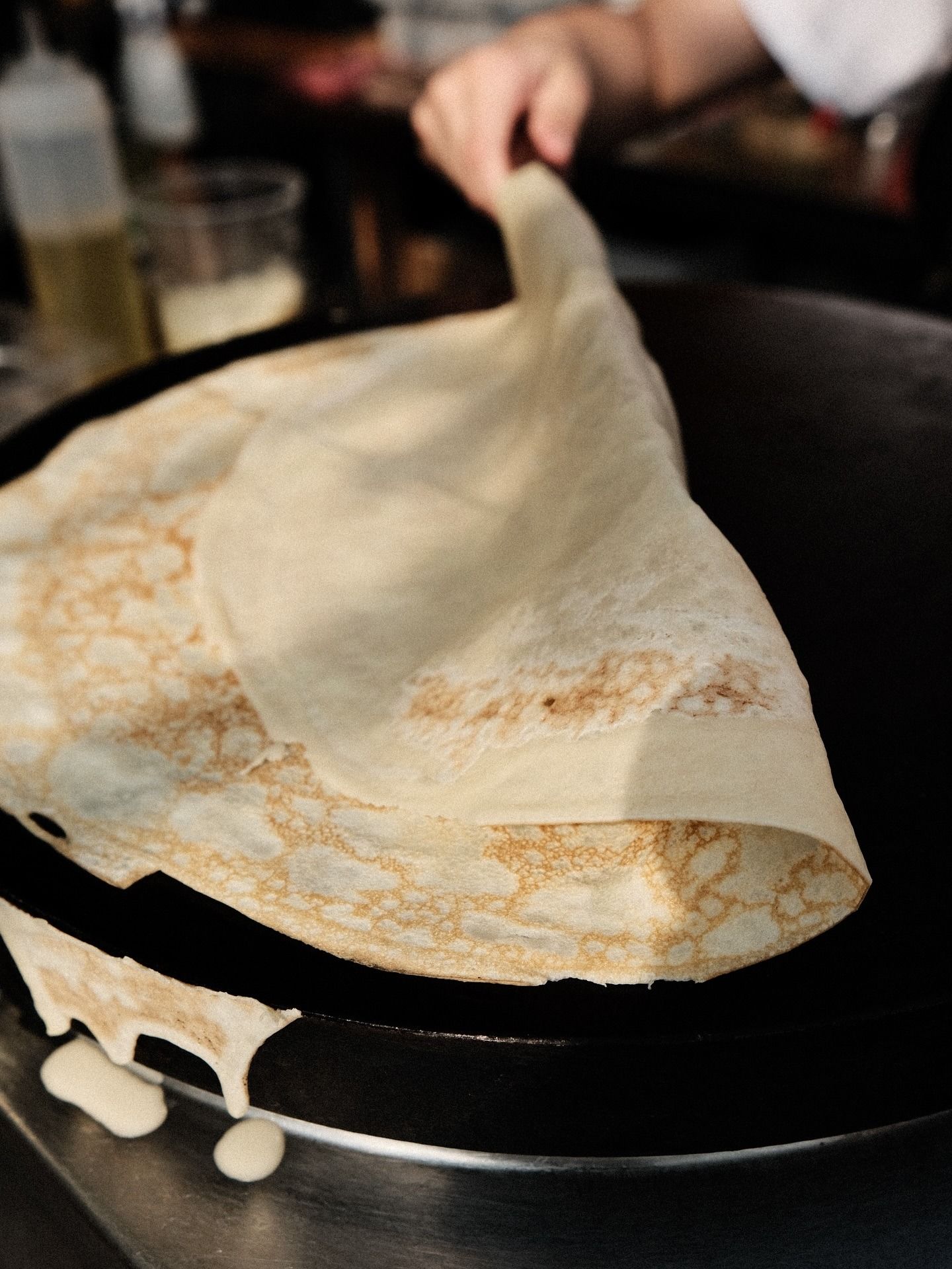 Crêpe pliée dans une poêle noire, la pâte dégoulinant sur le bord.