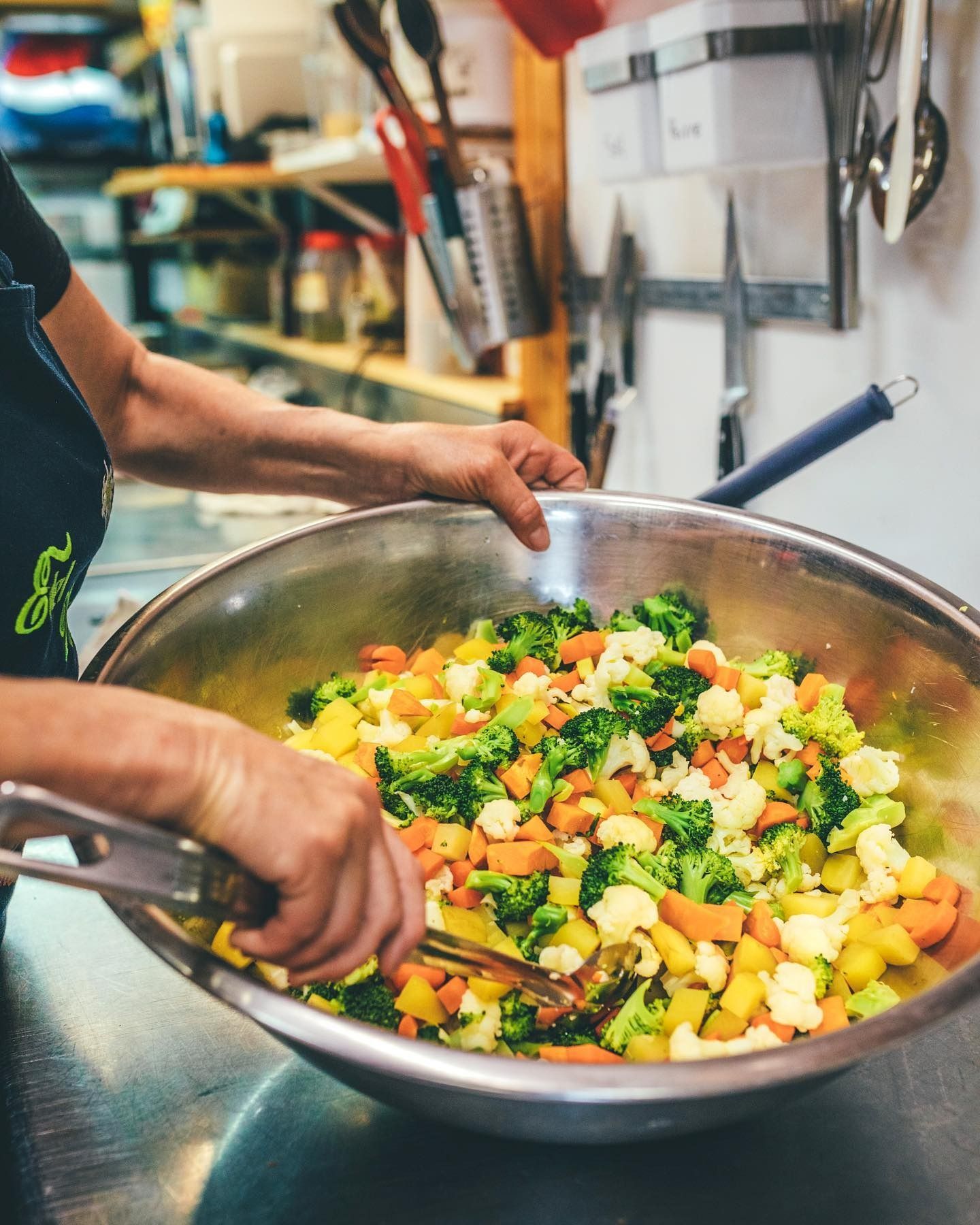 Une personne remuant un grand bol de légumes colorés hachés dans une cuisine