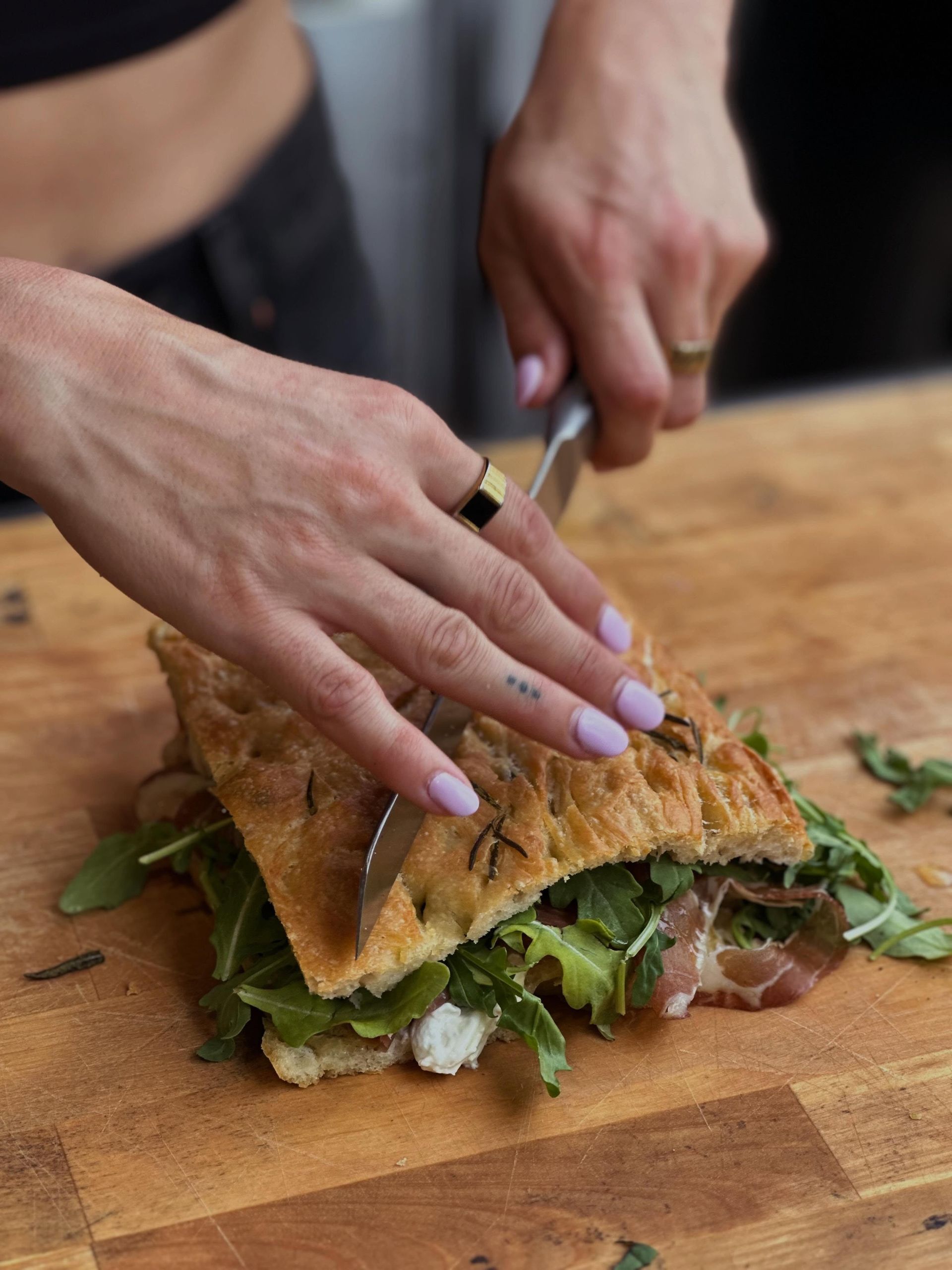 Des mains qui découpent un sandwich grillé sur une planche à découper en bois