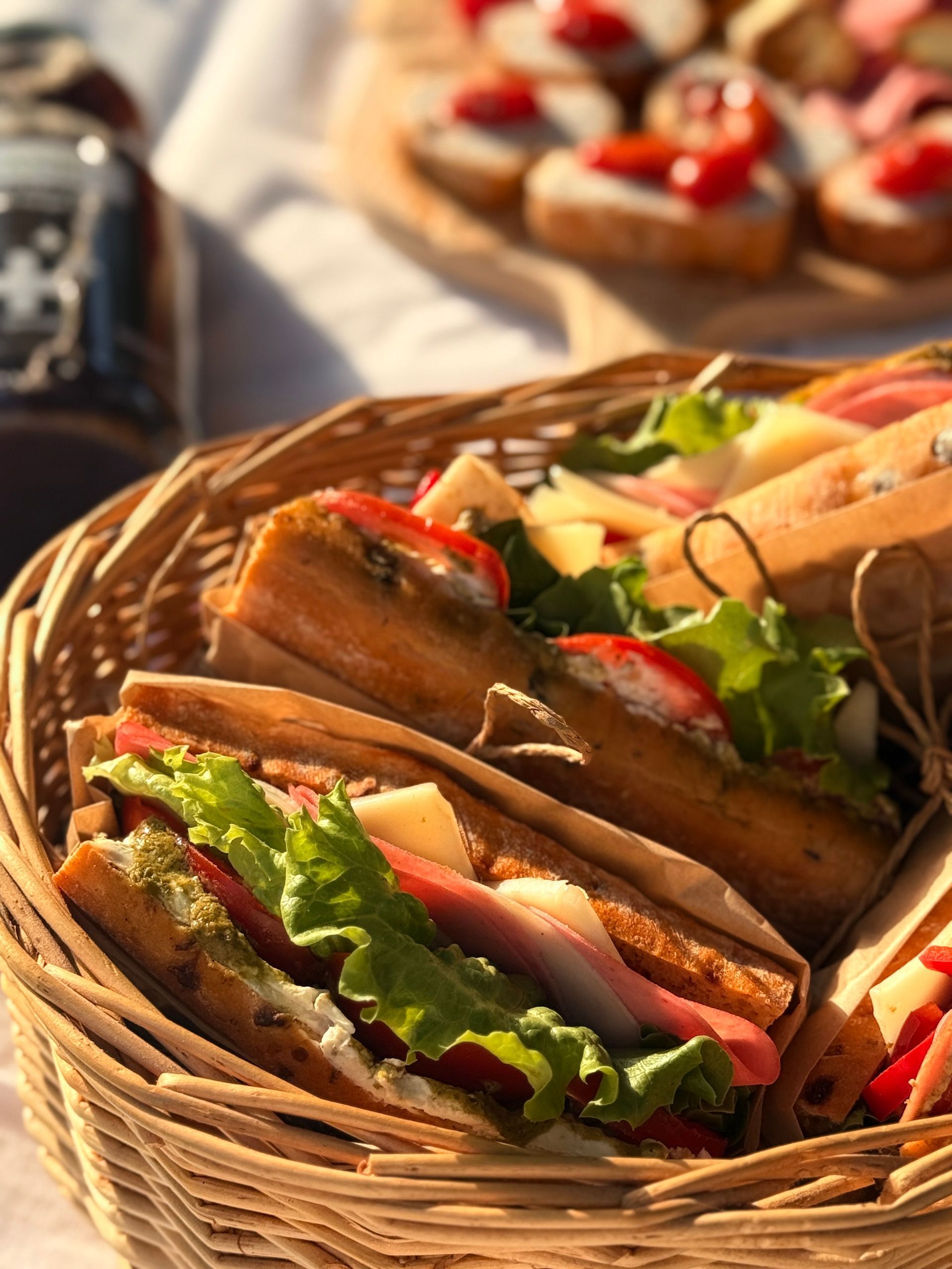 Un panier de sandwichs grillés avec de la laitue, des tomates et du jambon sur une table baignée de soleil.