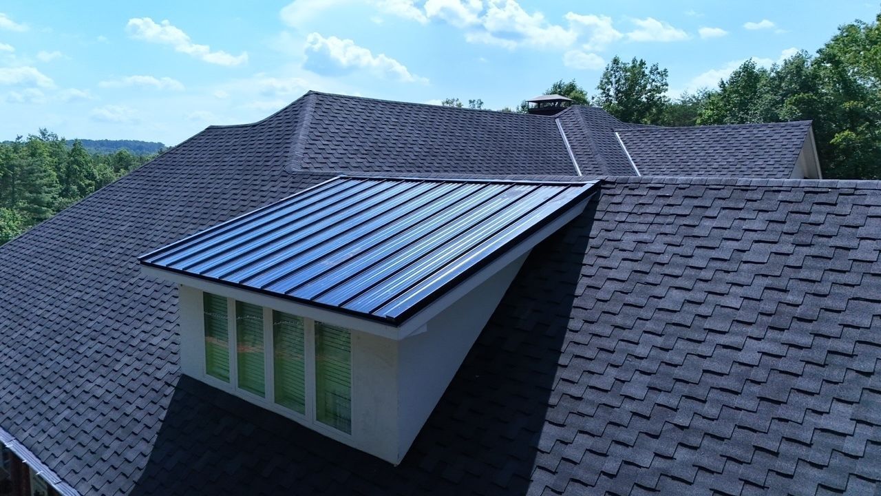 Rooftop dormer with blue metal roof on a shingled house under a bright sky