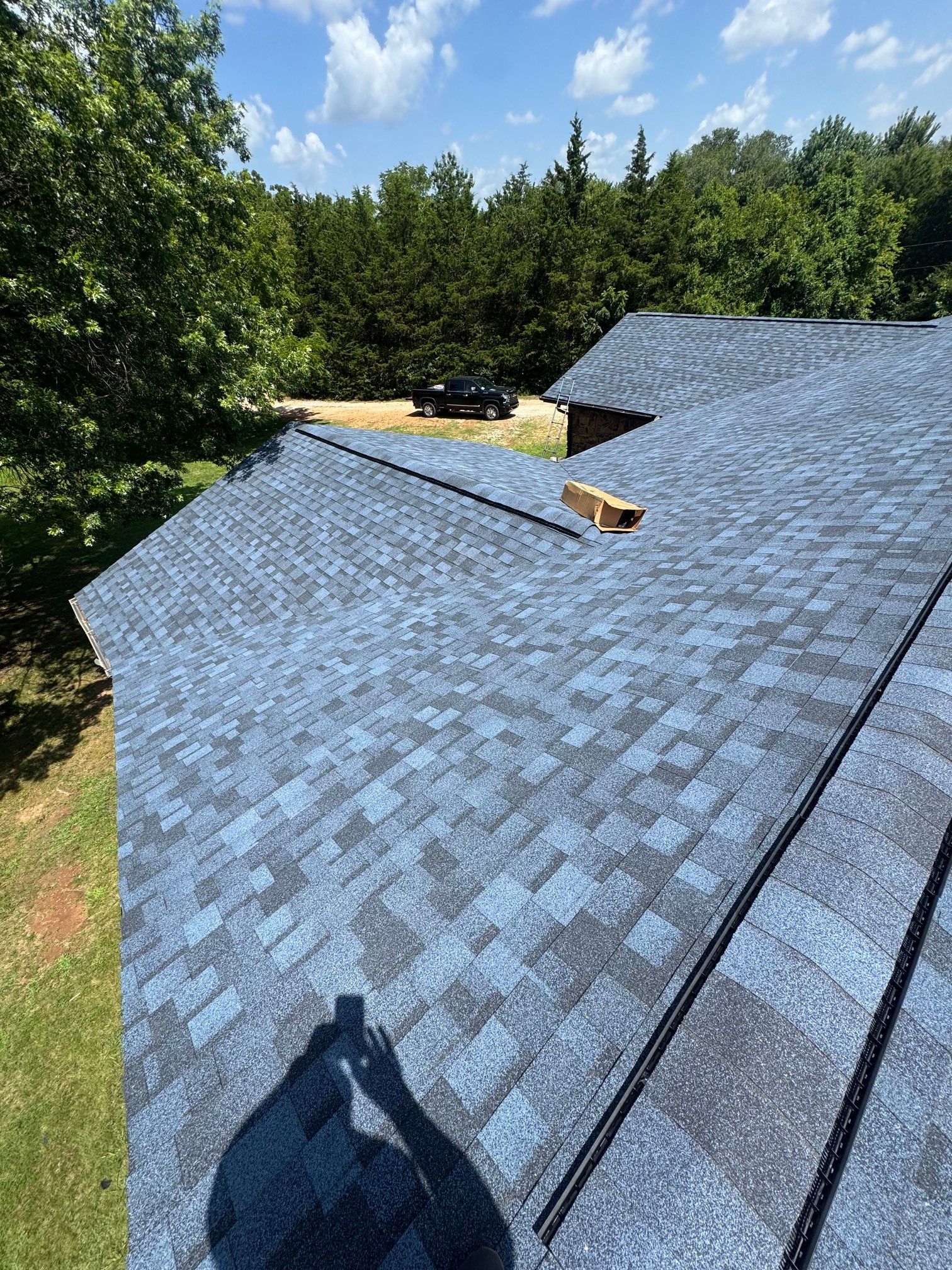 Roof under construction with blue shingles, skylights, and trees in the background