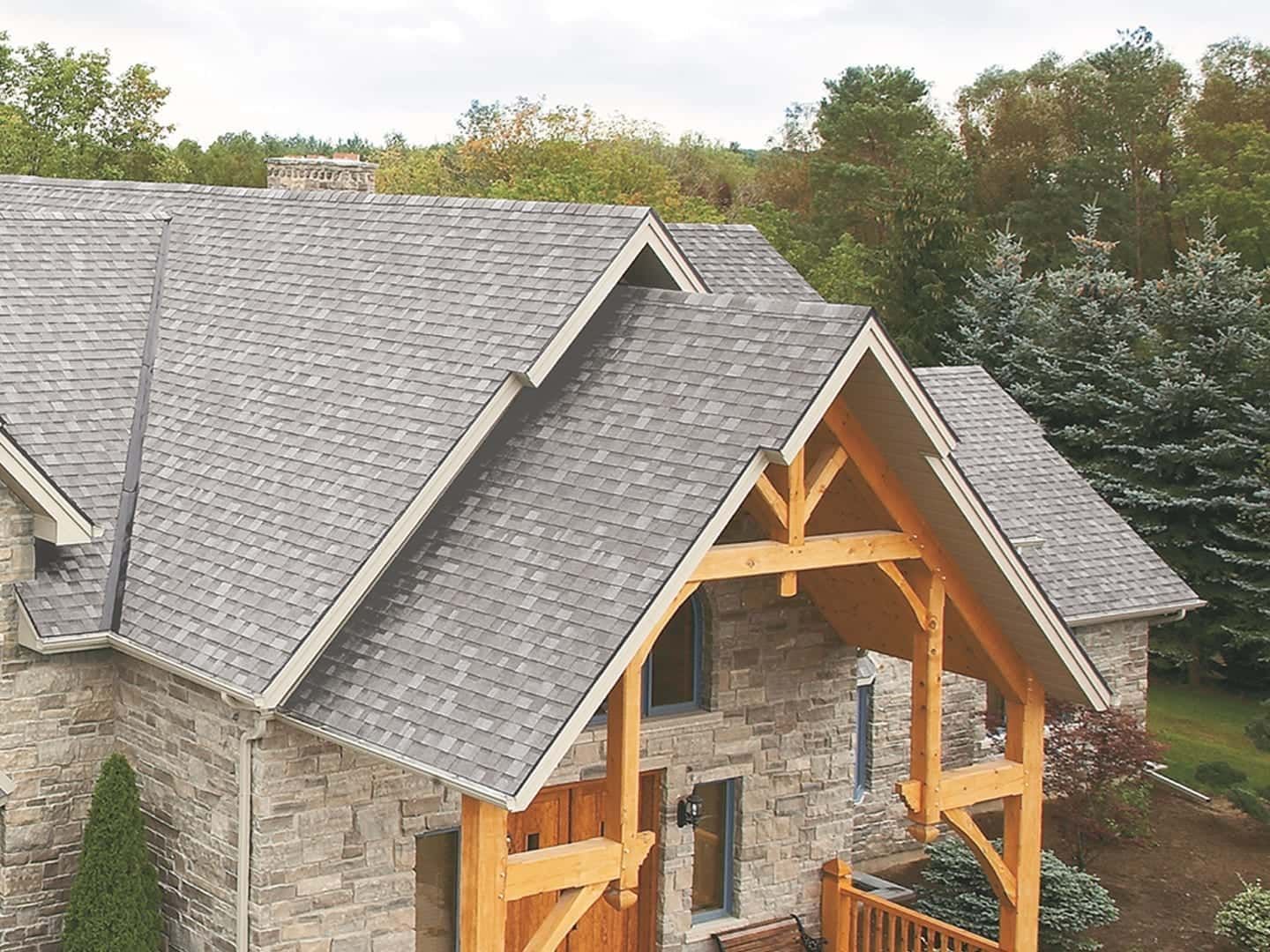 Stone house with gray shingled roof and timber porch under construction