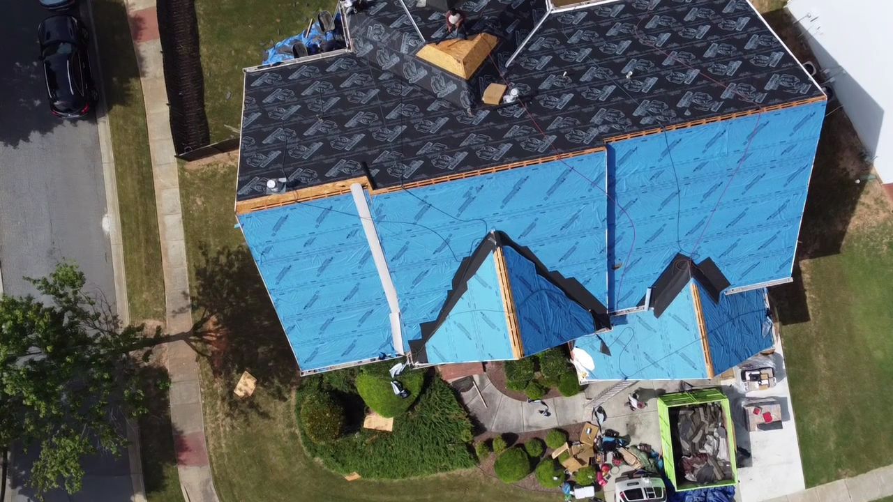 Aerial view of a blue-roofed house with a small yard and driveway.