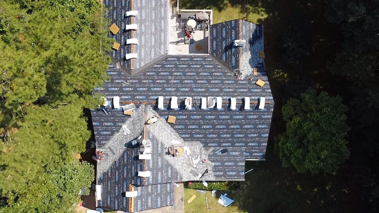 Aerial view of a gray-shingled house roof surrounded by trees and patio furniture.