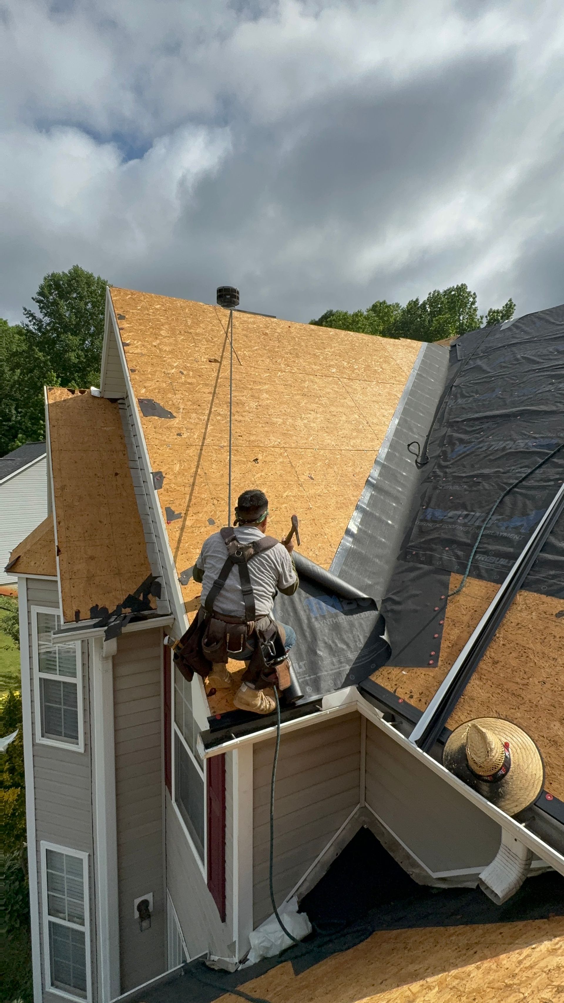 Worker securing roof shingles on a steep house roof under cloudy sky
