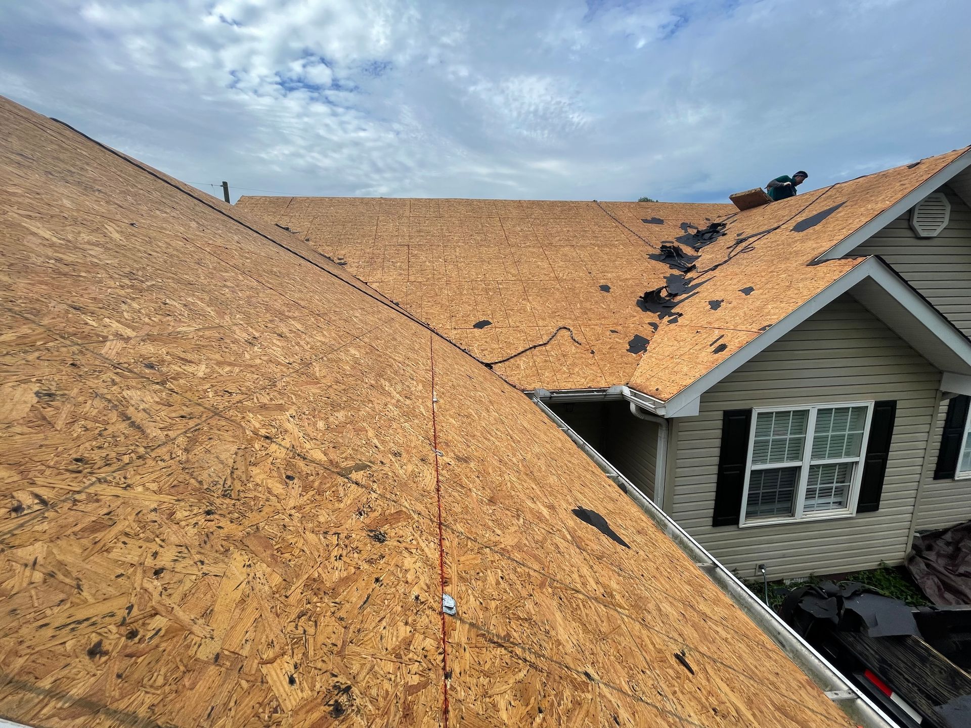 Roof underlayment exposed after shingles removed, with a house wall and scattered debris visible.