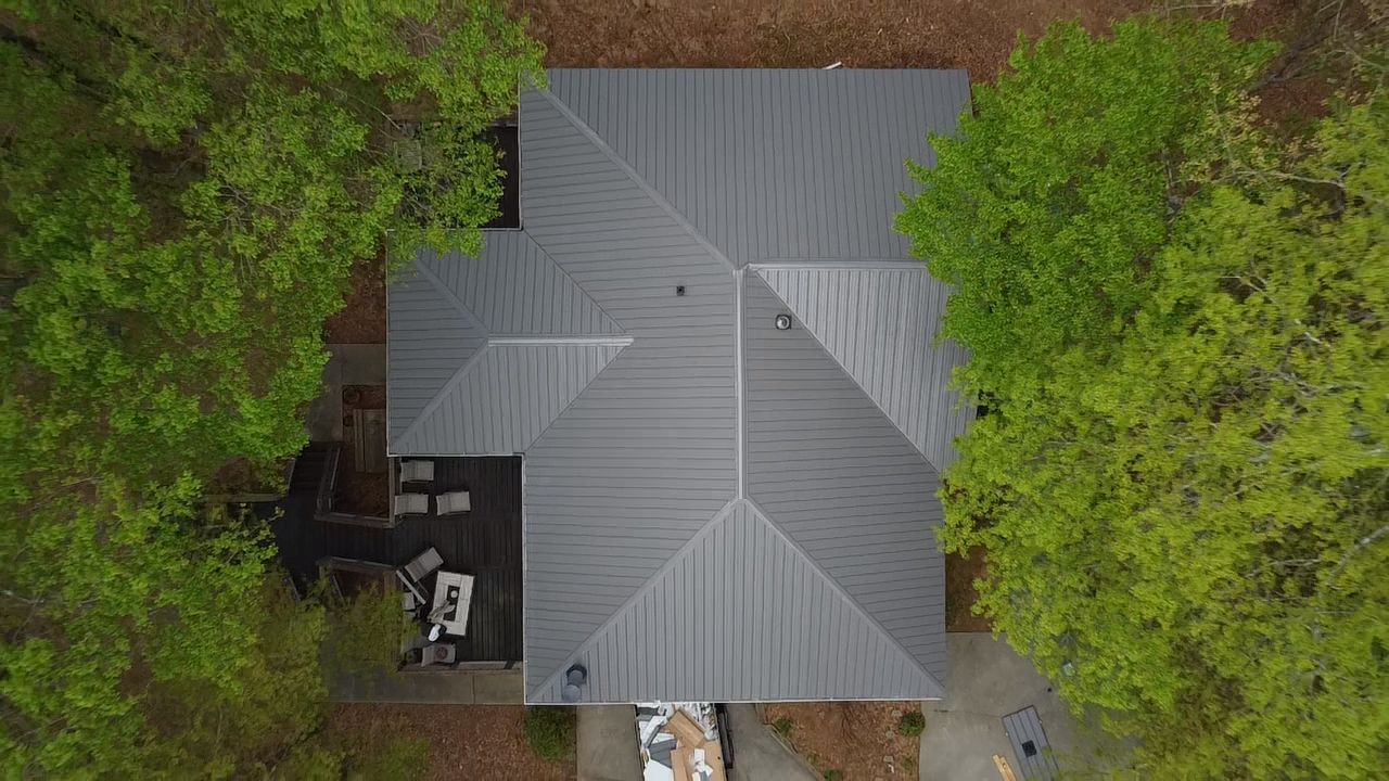 Aerial view of a gray-roofed house surrounded by dense green trees.