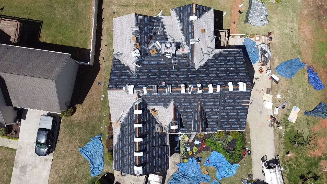 Aerial view of a roof under construction with solar panels, ladders, and blue tarps around it
