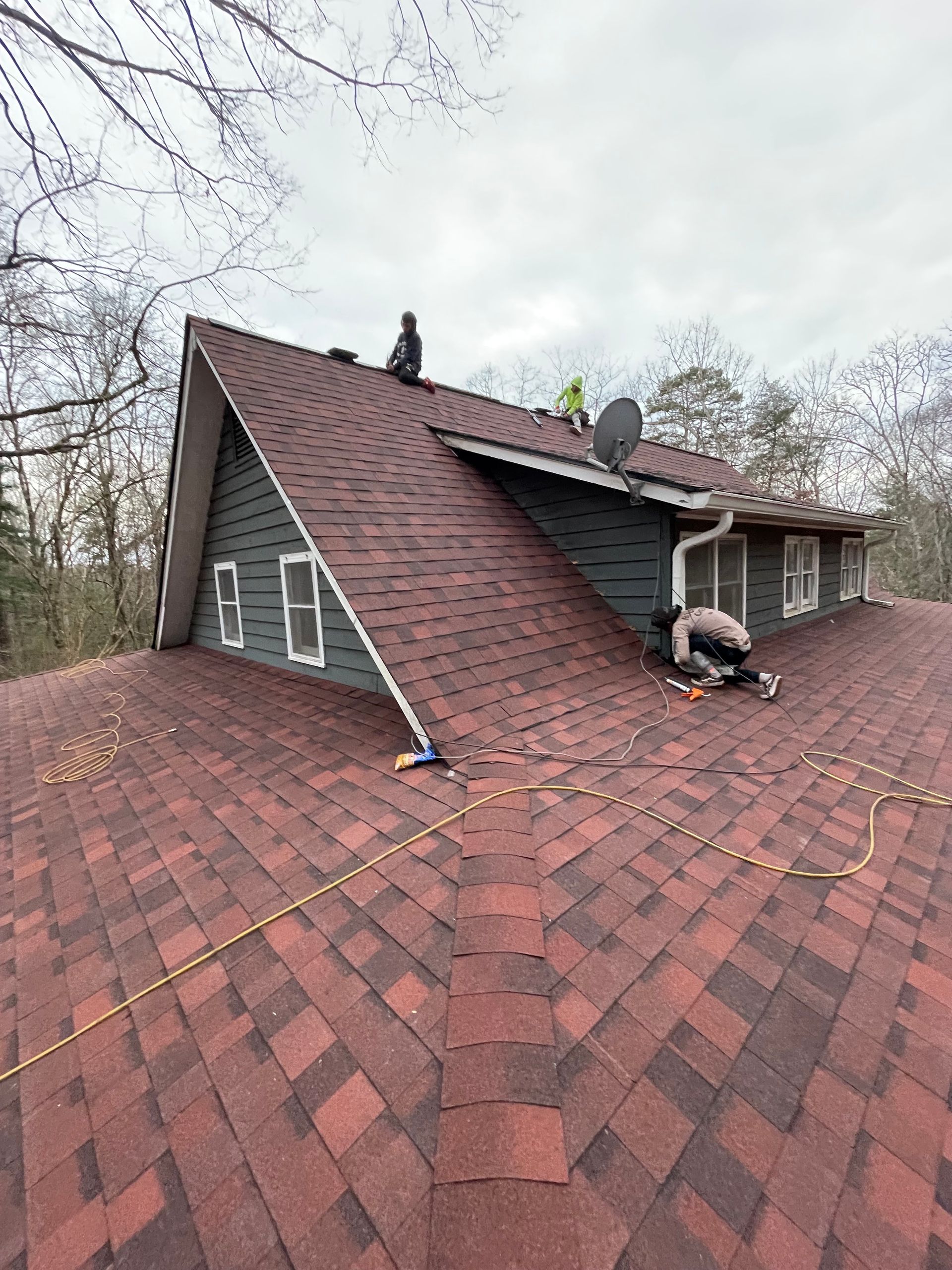 Roofers repairing a steep red shingle roof on a house with a dormer window