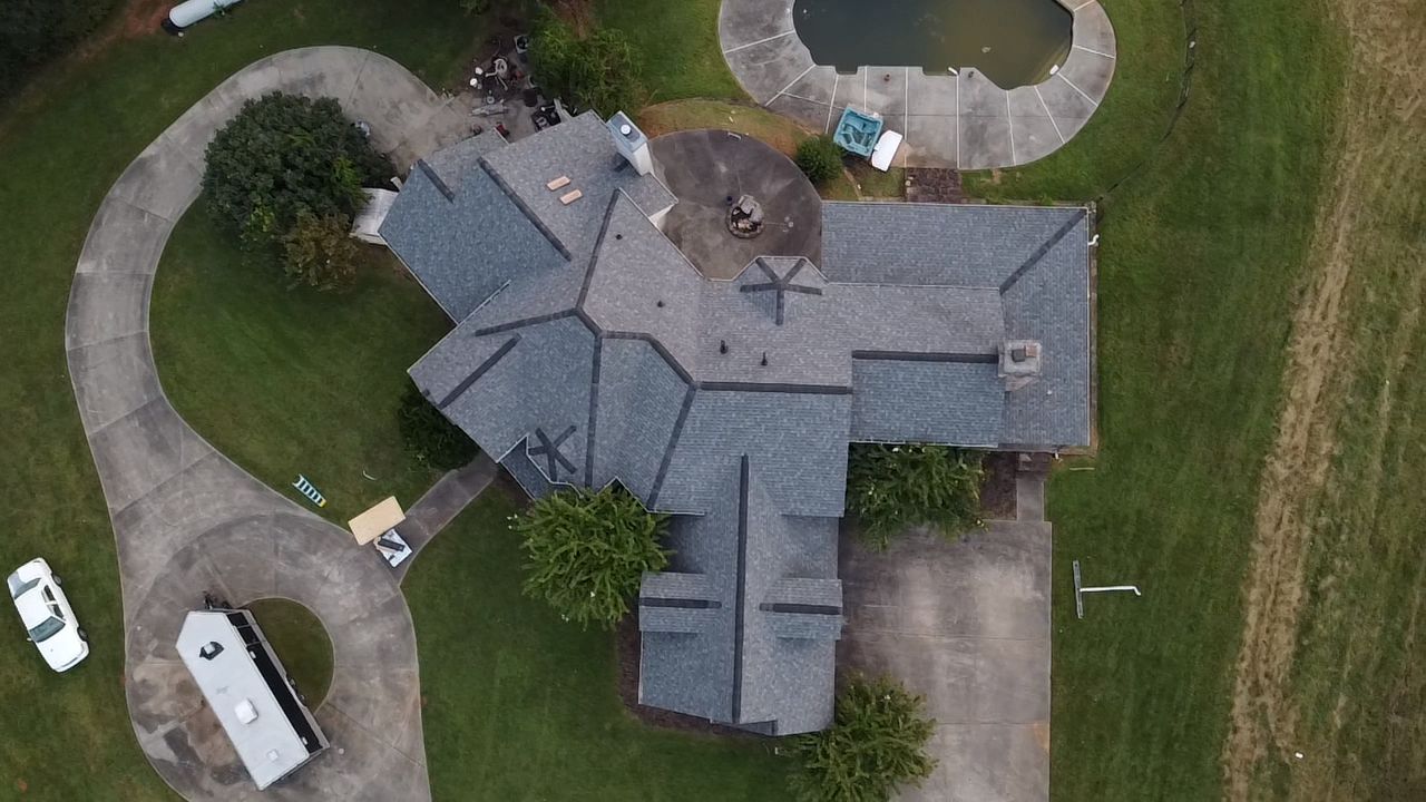 Aerial view of a gray-roofed house with curved driveway and parked vehicles on green lawn