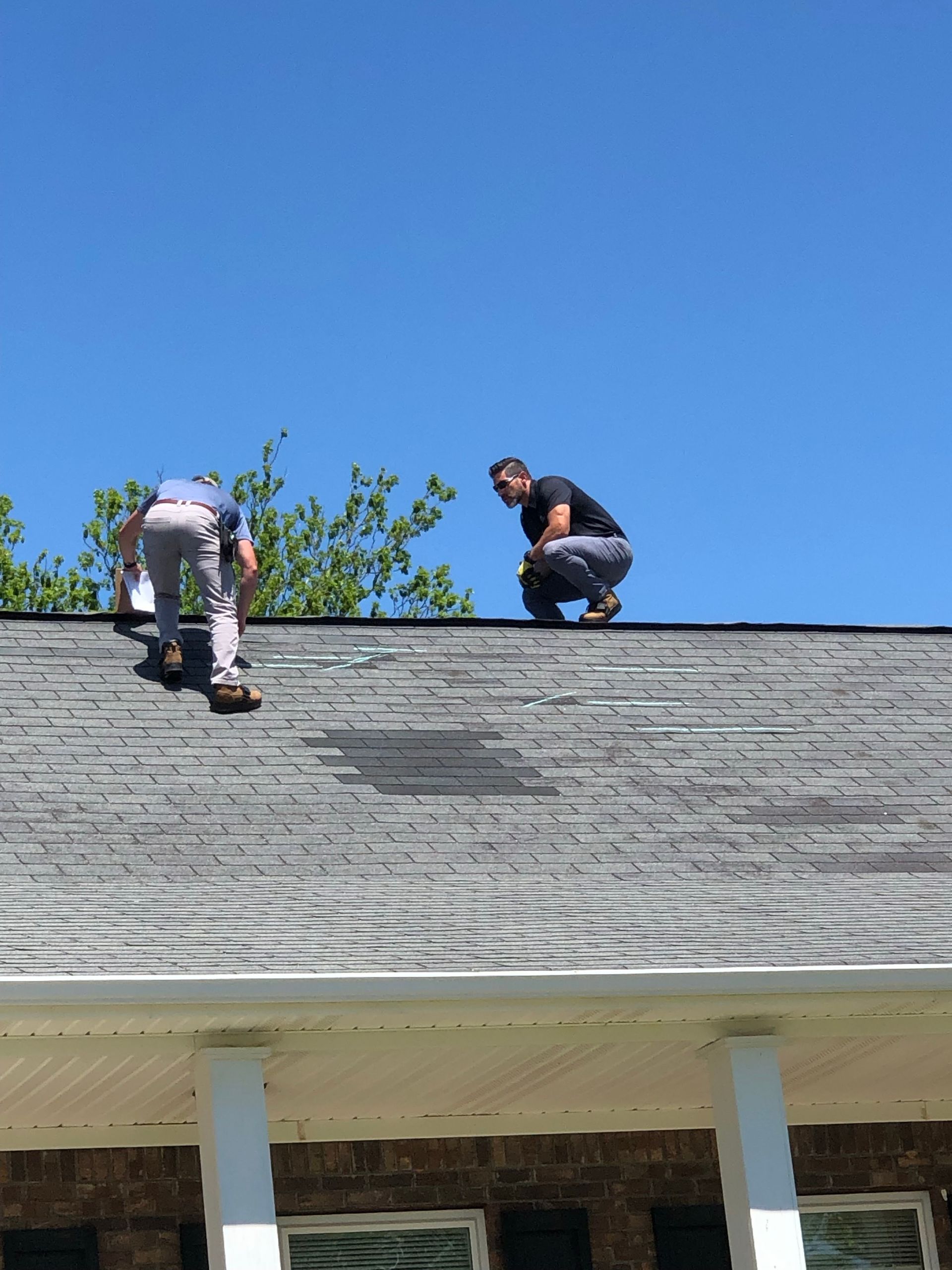 Two workers on a roof repairing shingles under a clear blue sky