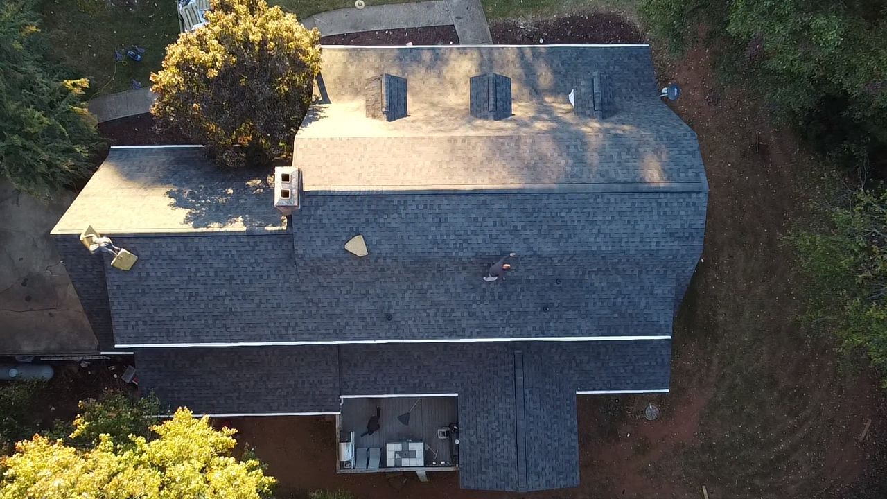 Aerial view of a gray-roofed house surrounded by trees and greenery.