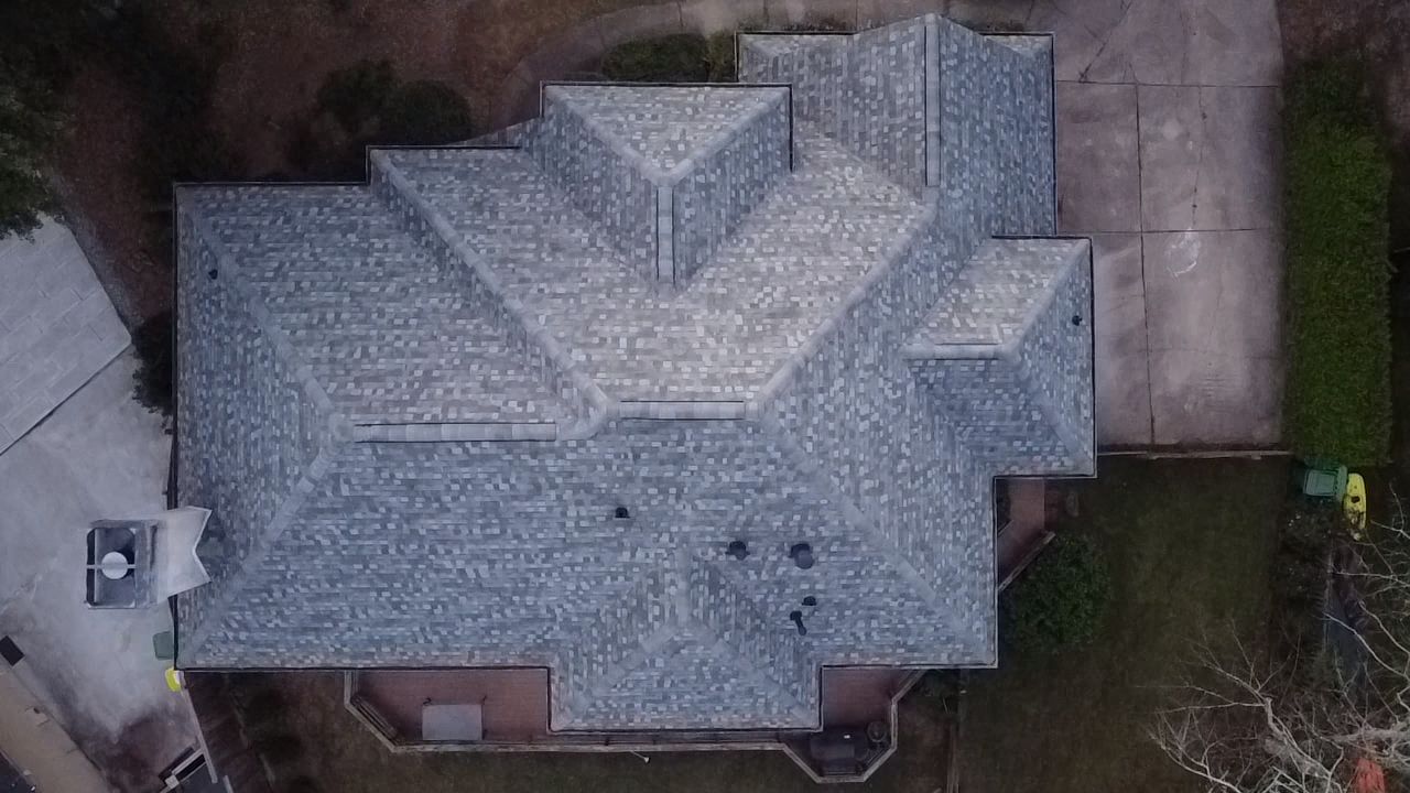 Aerial view of a house with a gray roof, surrounded by a driveway and trees.
