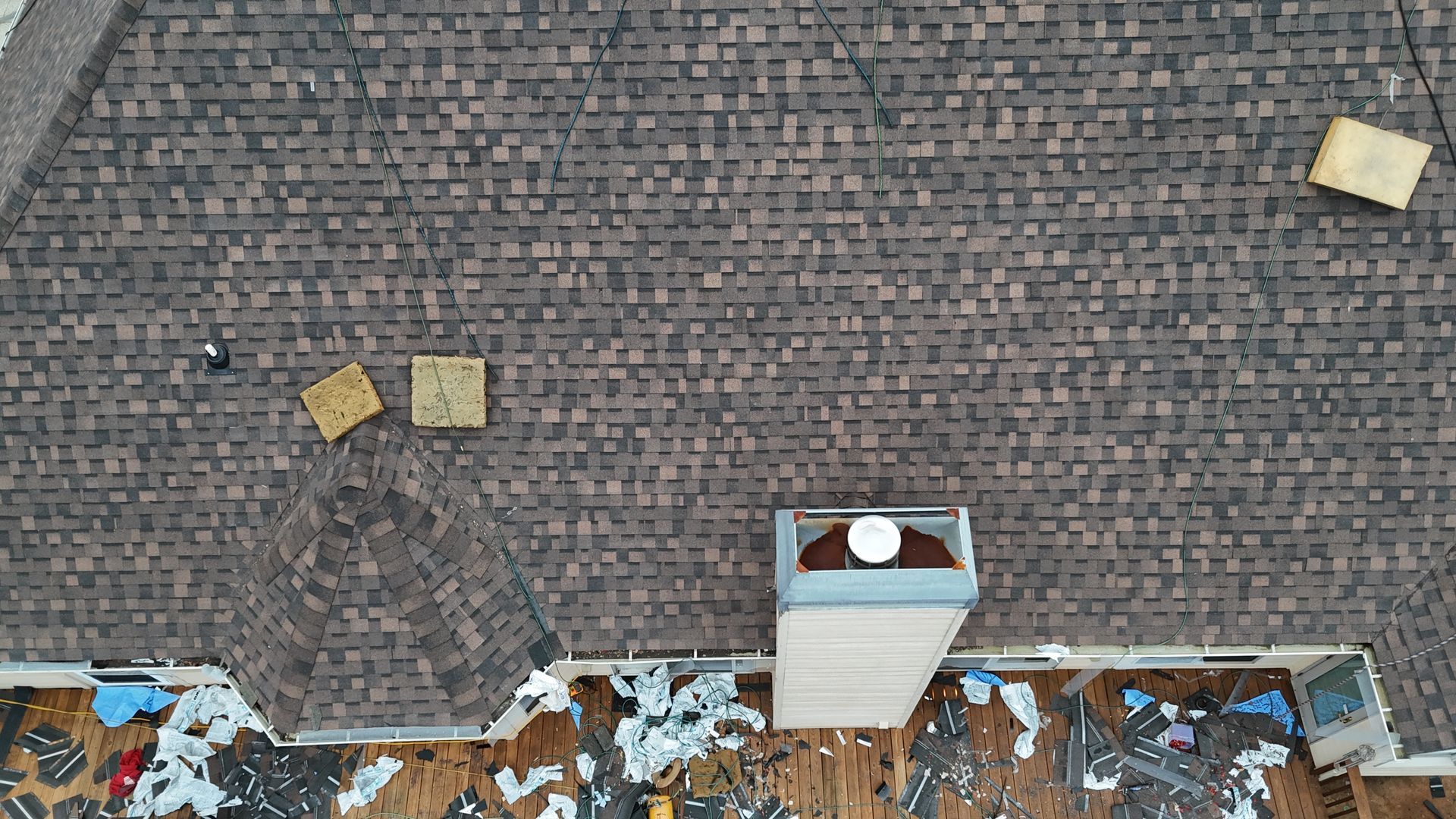 Overhead view of a dark shingled roof with debris and a small chimney vent near the bottom center