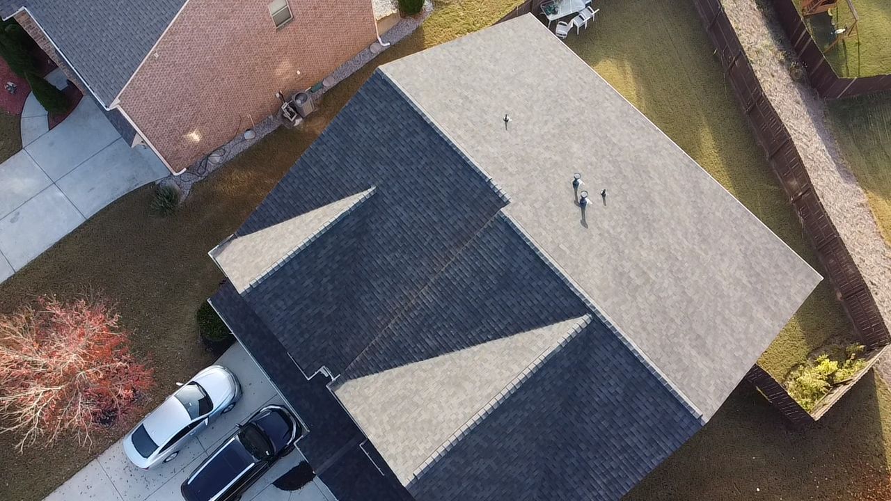 Aerial view of a house roof with two parked cars beside it and a yard with trees and grass.