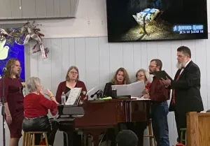 Choir singing beside a piano in a church, with a wall screen showing a butterfly image.