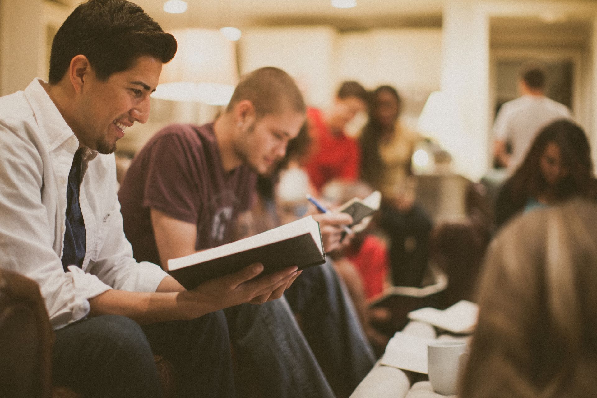 People seated in a waiting room, one reading a tablet while others look at phones.