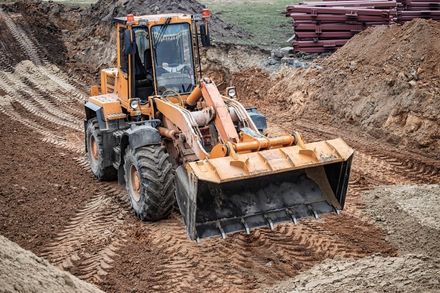 Yellow front-end loader parked in a muddy, excavated trench on a construction site.