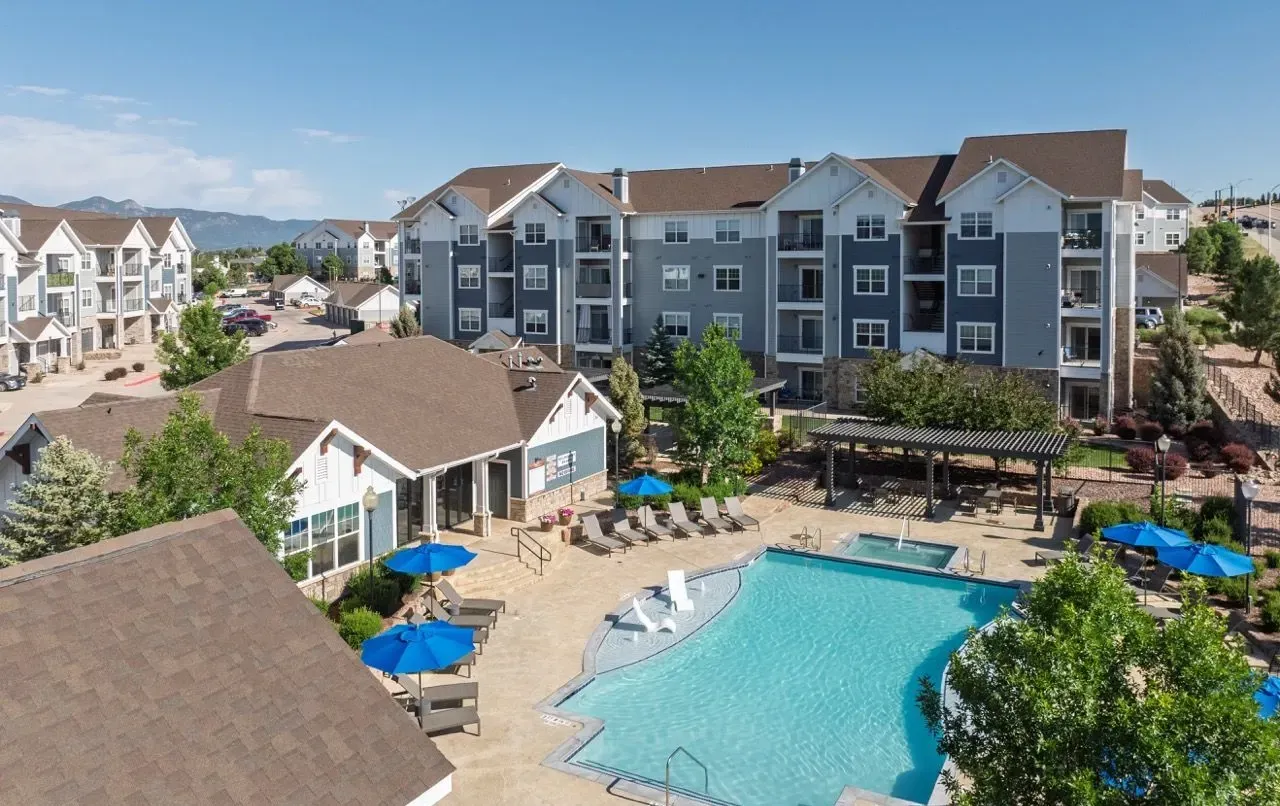 Outdoor swimming pool and lounge area with apartment buildings in the background.