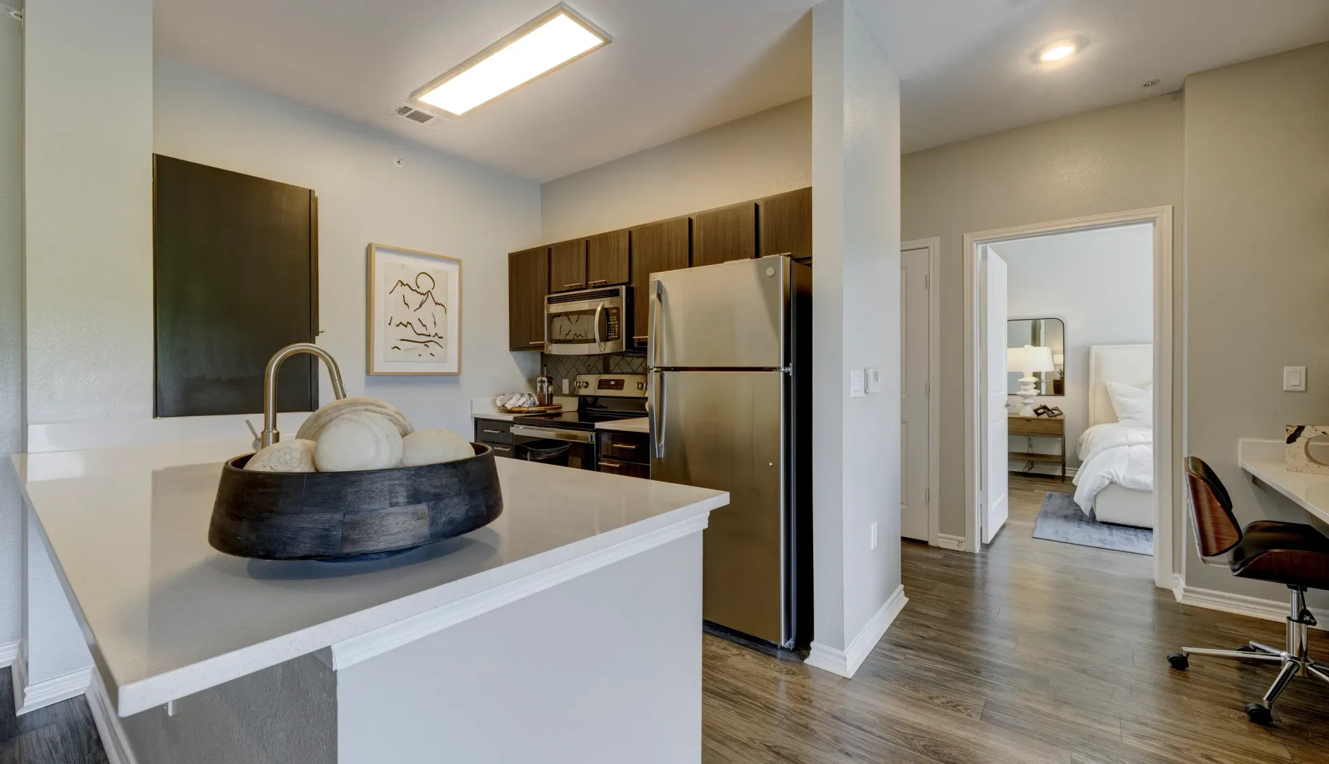 Kitchen with island and stainless steel appliances, view into bedroom.