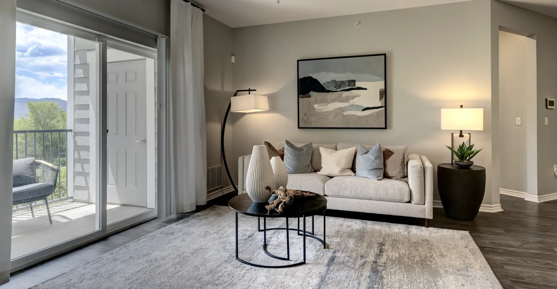 Modern living room with a couch, coffee table, floor lamp, and balcony access.