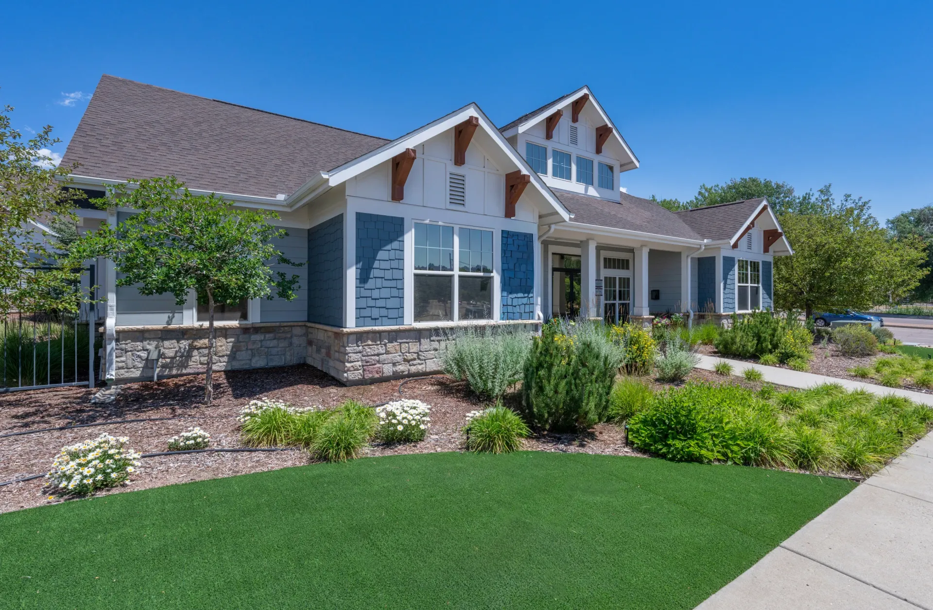 Exterior of a blue and grey building with stone accents and white trim, surrounded by manicured landscaping and a bright blue sky.