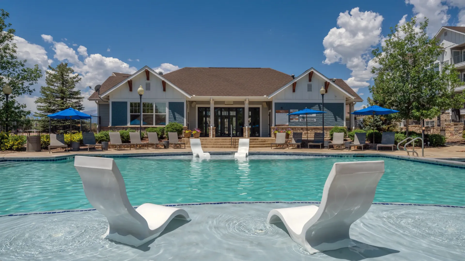 Swimming pool with lounge chairs and a clubhouse in the background.