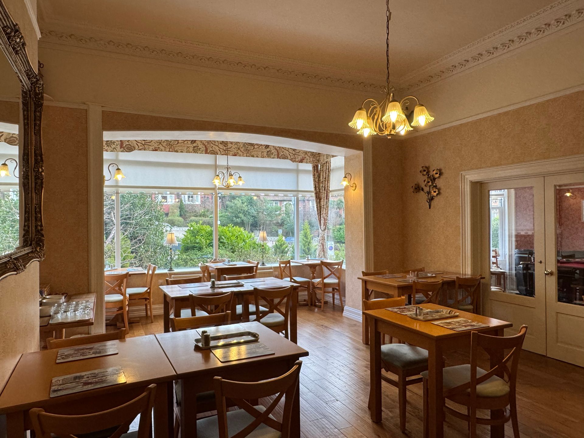 Restaurant dining area with tables, chairs, and a large bay window overlooking greenery.