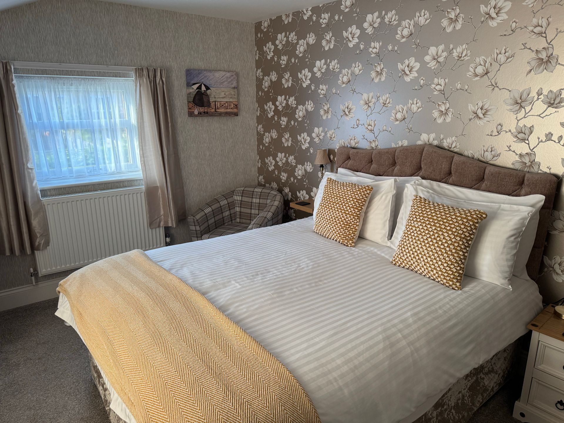 Bedroom with a double bed, floral wallpaper, window, and small chair.