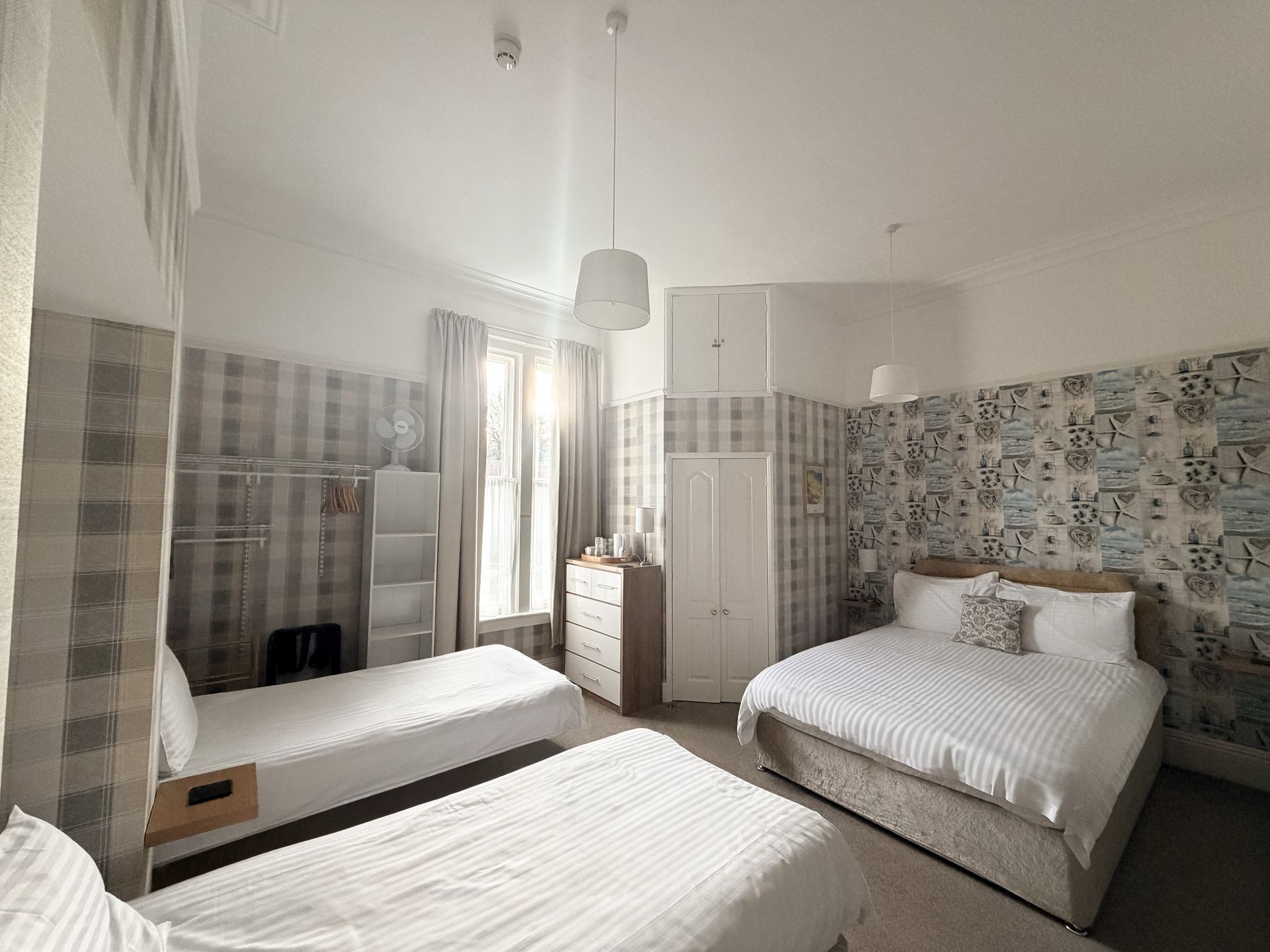 Bedroom with two twin beds, one double bed, a dresser, and a wardrobe. Bright and airy room with patterned wallpaper.