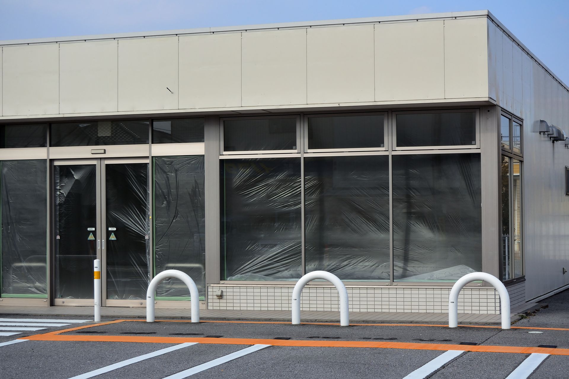Closed storefront with boarded-up windows and metal barriers in front, under a clear sky. Closed storefront with boarded-up windows and metal barriers in front, under a clear sky.